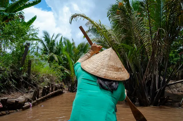 A traditional wooden sampan waiting in a palm-lined canal