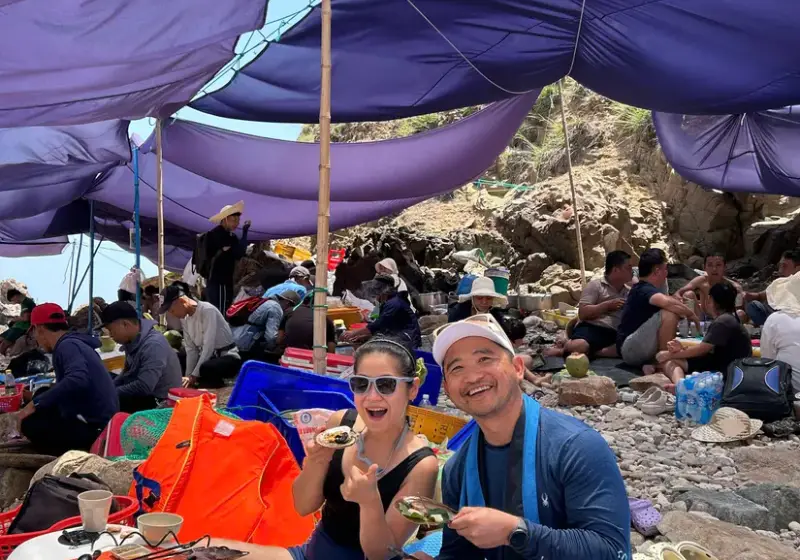 Guests eating a seafood lunch on mats under tarpaulins on the island rocks
