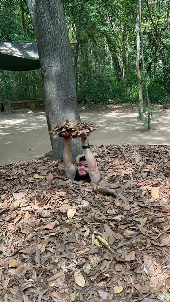 Guest demonstrating a hidden, camouflaged trapdoor at Củ Chi