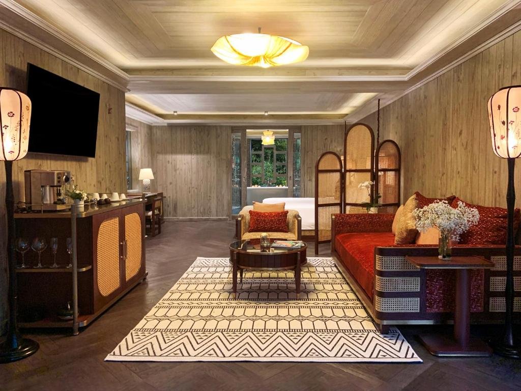 A sitting area with a red cushioned daybed, lantern floor lamps and a patterned rug, a coffee bar with glasses on the left, and the bed half-hidden behind arched rattan screens