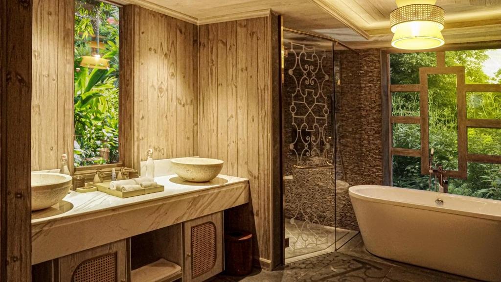 A timber-lined bathroom with two stone bowl basins, a glass walk-in shower with a wrought-iron pattern, and a freestanding bathtub beneath a large window onto the garden
