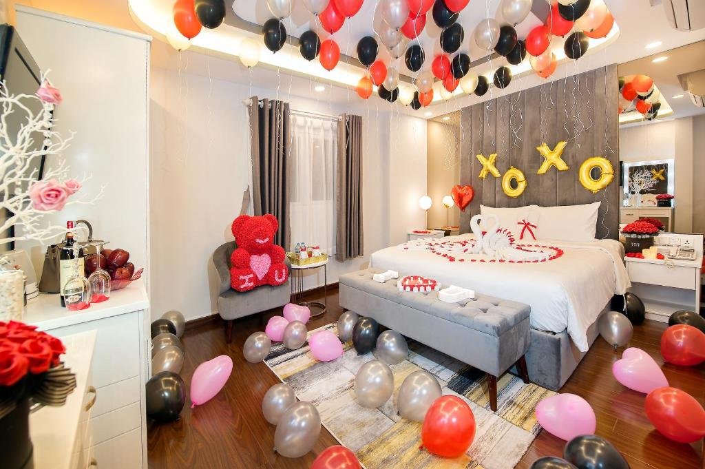 The room decorated with red, black, silver and pink balloons, gold XOXO letters over the bed, towel swans in a heart of rose petals, and a red rose teddy bear on the armchair