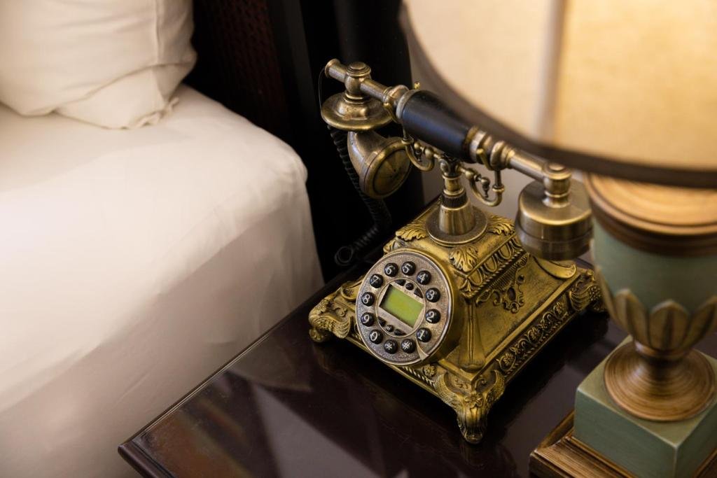 A brass antique-style telephone on the dark bedside table, beside the bed and under a lamp