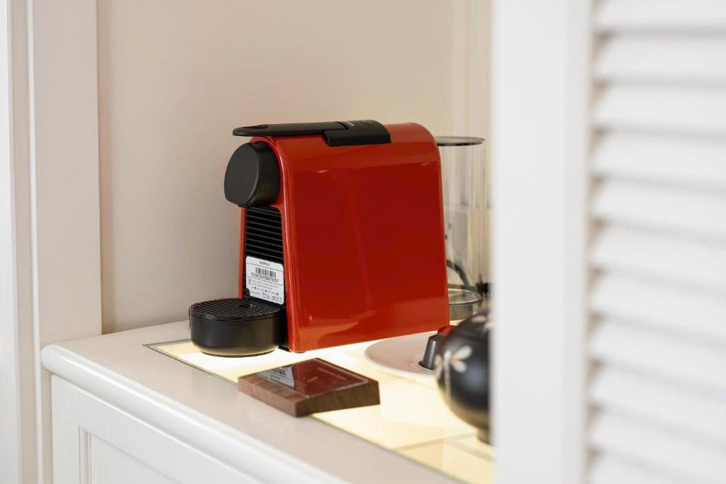 A red capsule coffee machine on a lit white shelf beside a louvred cabinet door