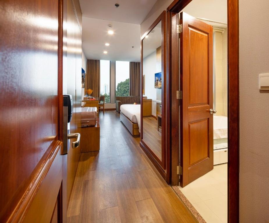 The room from the entrance: a wood-floored hallway past a luggage bench to the bed, sofa and window, with the bathroom and its bathtub through a door on the right