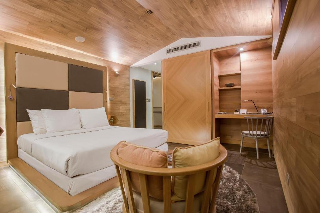 The bed and checkerboard headboard, a herringbone-panelled sliding wardrobe, a built-in desk with a lamp and telephone, and a curved wooden armchair with cushions in the foreground