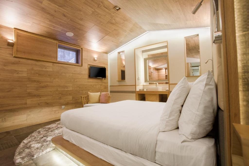 The bed seen from the pillow end: timber walls and ceiling, a TV and armchair on the far wall, and the open vanity with its tall mirrors