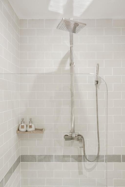A square rain shower head and hand shower against white subway tiles, with refillable toiletry bottles on a small shelf