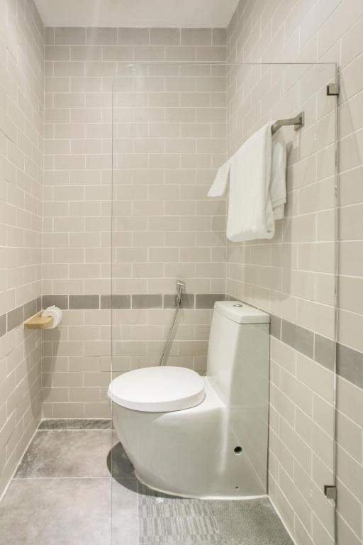 A white toilet with a bidet spray behind a glass screen, a towel on a rail and a wooden toilet-roll holder on subway tiles