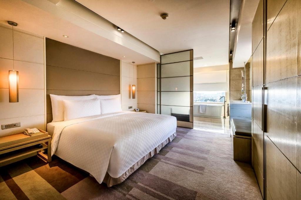 The bedroom seen towards the bathroom: the king bed on the left, wood-panelled wardrobes on the right, and the freestanding bathtub against a window beyond