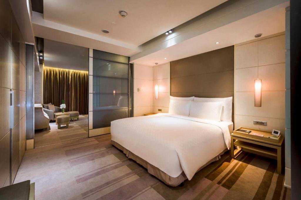 The Nikko Club Executive Suite at Hotel Nikko Saigon: a king bed against a tall padded headboard with pendant lights, and through a frosted glass partition the living room with armchairs and ottomans