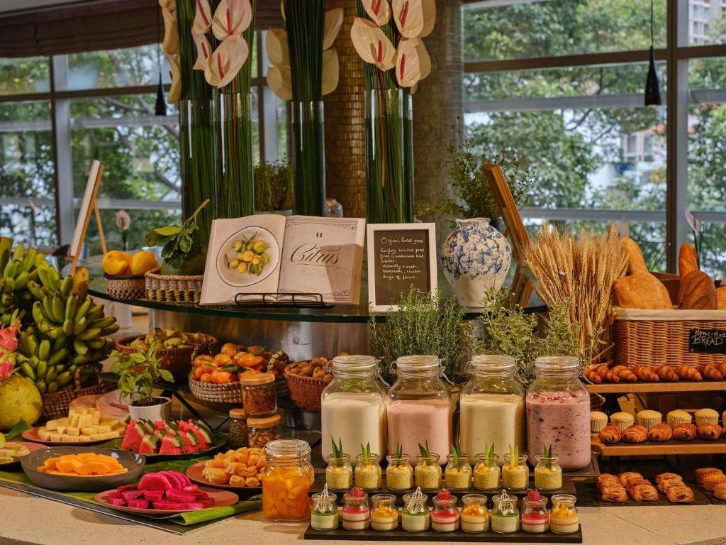 A breakfast buffet with bananas and tropical fruit, jars of yoghurt and smoothies, small dessert pots, baskets of bread and croissants, and vases of anthurium