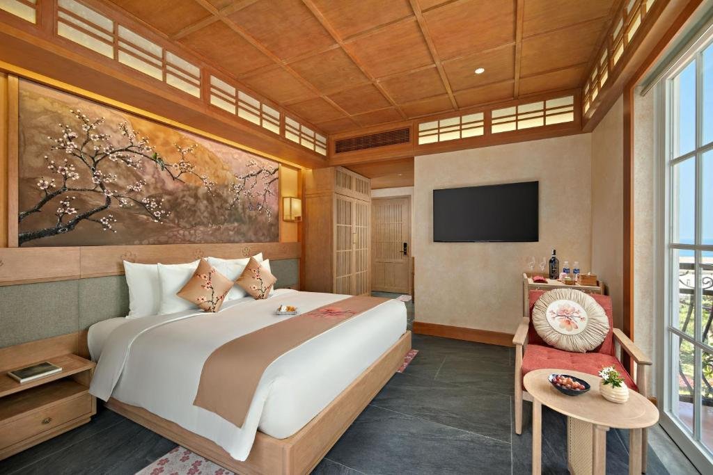 The same room from the window end: the blossom mural running the length of the bed wall, a wall-mounted flat-screen opposite, a minibar console beneath it, and an armchair with a round table