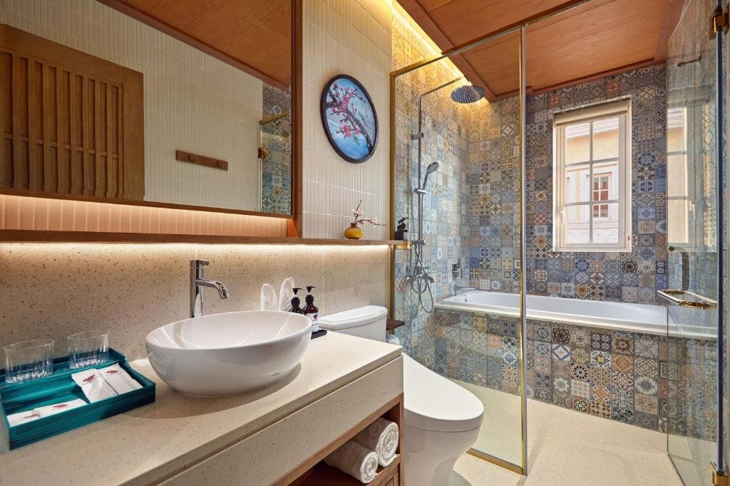 The tub set under a window at the end of the bathroom, the rainfall shower beside it, and the vanity with folded towels on the shelf below