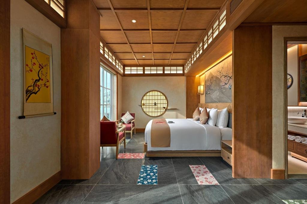 The room seen from the entrance: a yellow blossom scroll on the wall, the bed and round lattice window beyond, blossom-patterned floor tiles, and the bathroom vanity through the doorway on the right