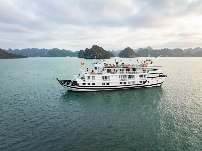 Cozy Grand under an overcast sky with the limestone islands of Halong Bay behind her