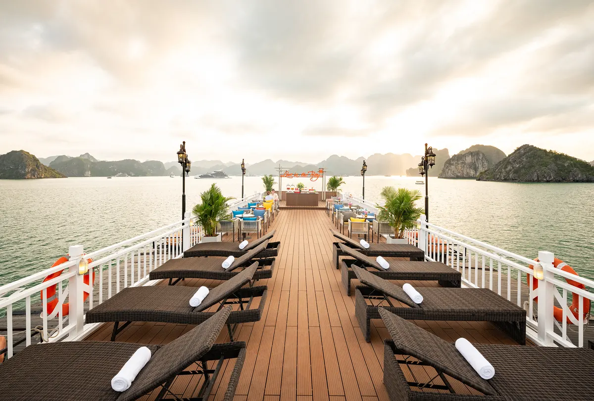 The sundeck of Cozy Grand looking aft: two rows of loungers along a teak deck under a wide grey sky