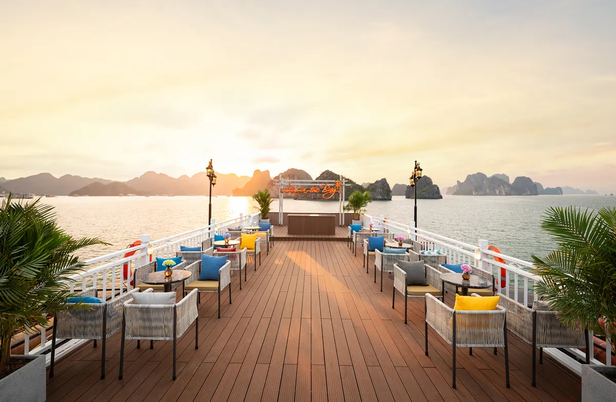 The sundeck bar at sunset, low tables and armchairs with yellow and blue cushions facing the water