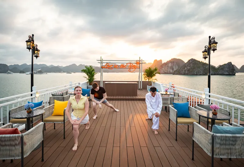 Guests following a Tai Chi instructor on the sundeck at sunrise, the bay flat and grey behind them