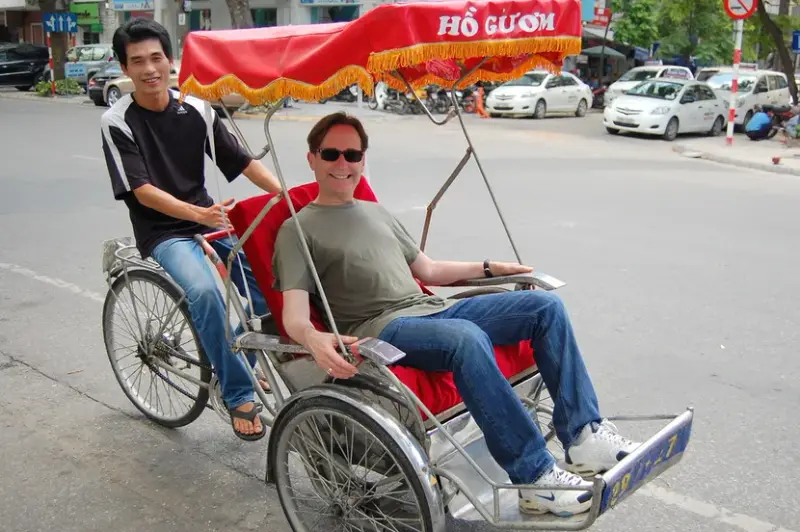 A cyclo driver pedalling a single guest along a wide Hanoi street under a red canopy