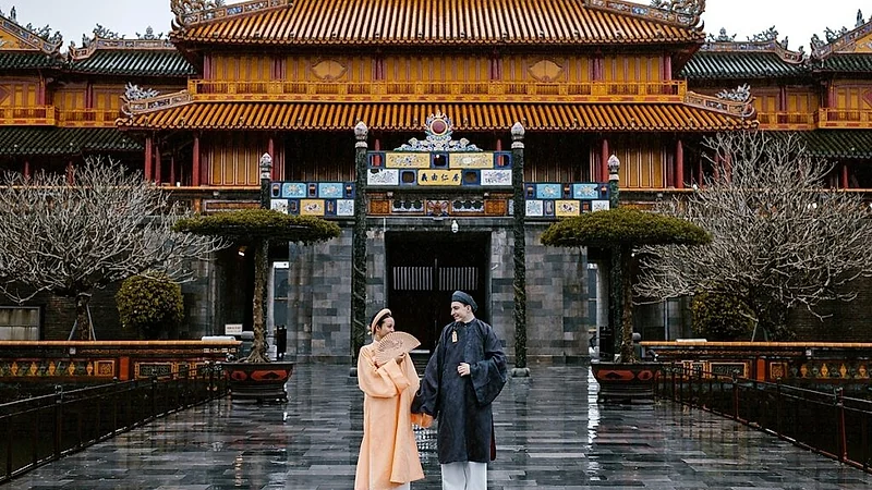 A couple in &aacute;o d&agrave;i before a palace hall in the Huế Imperial City