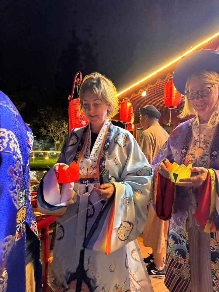 Two guests in Huế court robes holding lit paper lotus lanterns at the rail
