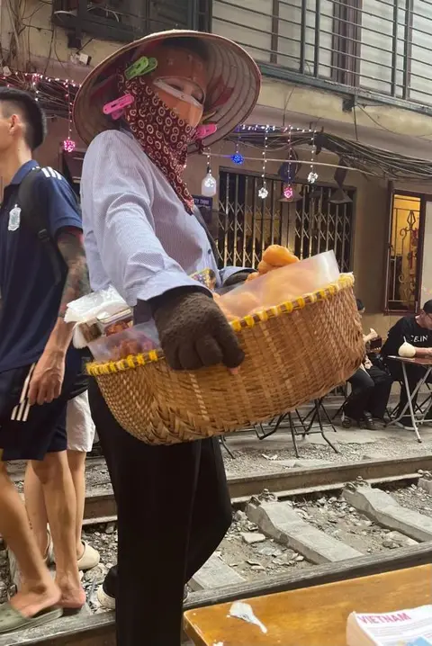 Street vendor carrying a basket along the railway in the Old Quarter