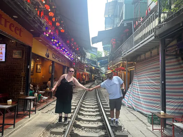Two guests standing on the rails of Train Street between cafes hung with red lanterns